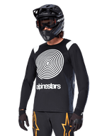 Alpinestars A-Supra Oscar langærmet trøje, MTB-cykeltrøje, sort og hvid, med et markant hvidt spiraldesign og Alpinestars-logo på brystet, båret med en sort full-face hjelm og goggles, performance-beklædning til mountainbike
