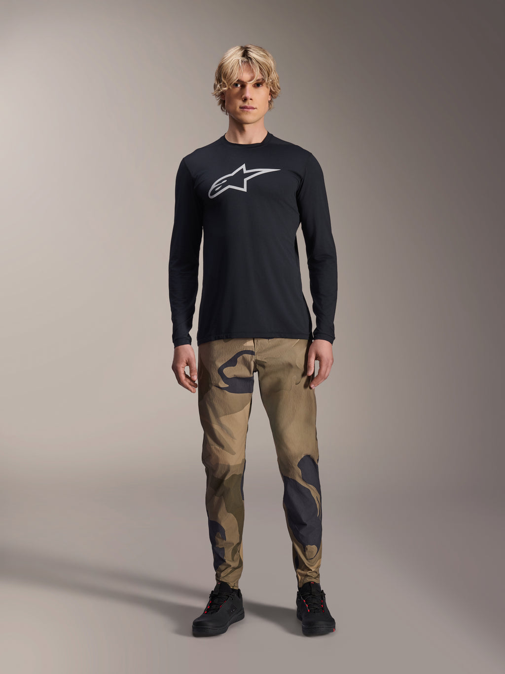 Alpinestars A-Dura Camo bukser, MTB-cykelbukser, brun og grøn camouflage, båret med en sort langærmet jersey og sorte sko, sporty mountainbike-stil med slidstærkt strækstof