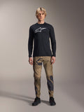 Alpinestars A-Dura Camo bukser, MTB-cykelbukser, brun og grøn camouflage, båret med en sort langærmet jersey og sorte sko, sporty mountainbike-stil med slidstærkt strækstof