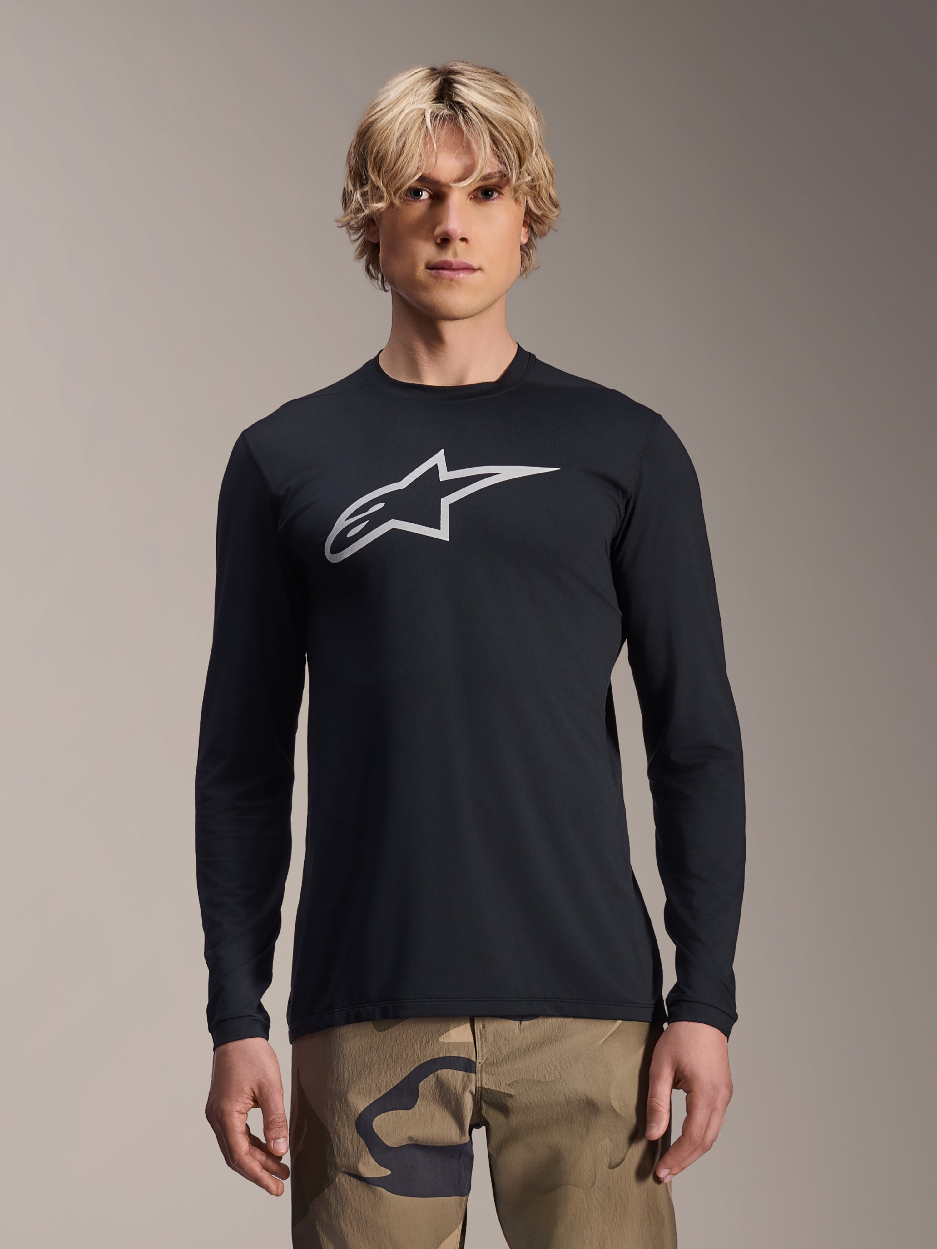 Alpinestars A-Dura Astar langærmet trøje, sort med sølvfarvet Astars-logo på brystet, båret af en model med camouflagebukser, afslappet MTB-performance-beklædning til mountainbike