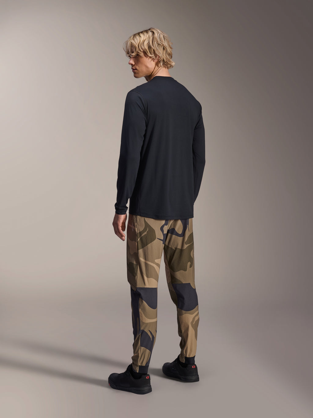 Alpinestars A-Dura Astar langærmet trøje, sort, rygvisning på en model, kombineret med camouflagebukser, afslappet MTB-performance-udstyr med længere drop hale og almindelig pasform