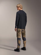 Alpinestars A-Dura Camo bukser, MTB-bukser, brun camouflage, båret med en sort langærmet trøje og sorte sneakers, set bagfra viser de tilspidsede ben og elastiske manchetter, performance-beklædning til off-road cykling