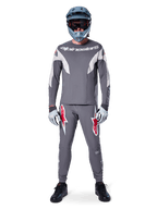 Rytter iført Alpinestars A-Supra Race Jersey - langærmet i mørkegrå, koordineret med matchende grå bukser med markante røde stjernelogoer, grå hjelm med goggles og lysegrå handsker, komplet MTB-racerudstyr til performance off-road cykling
