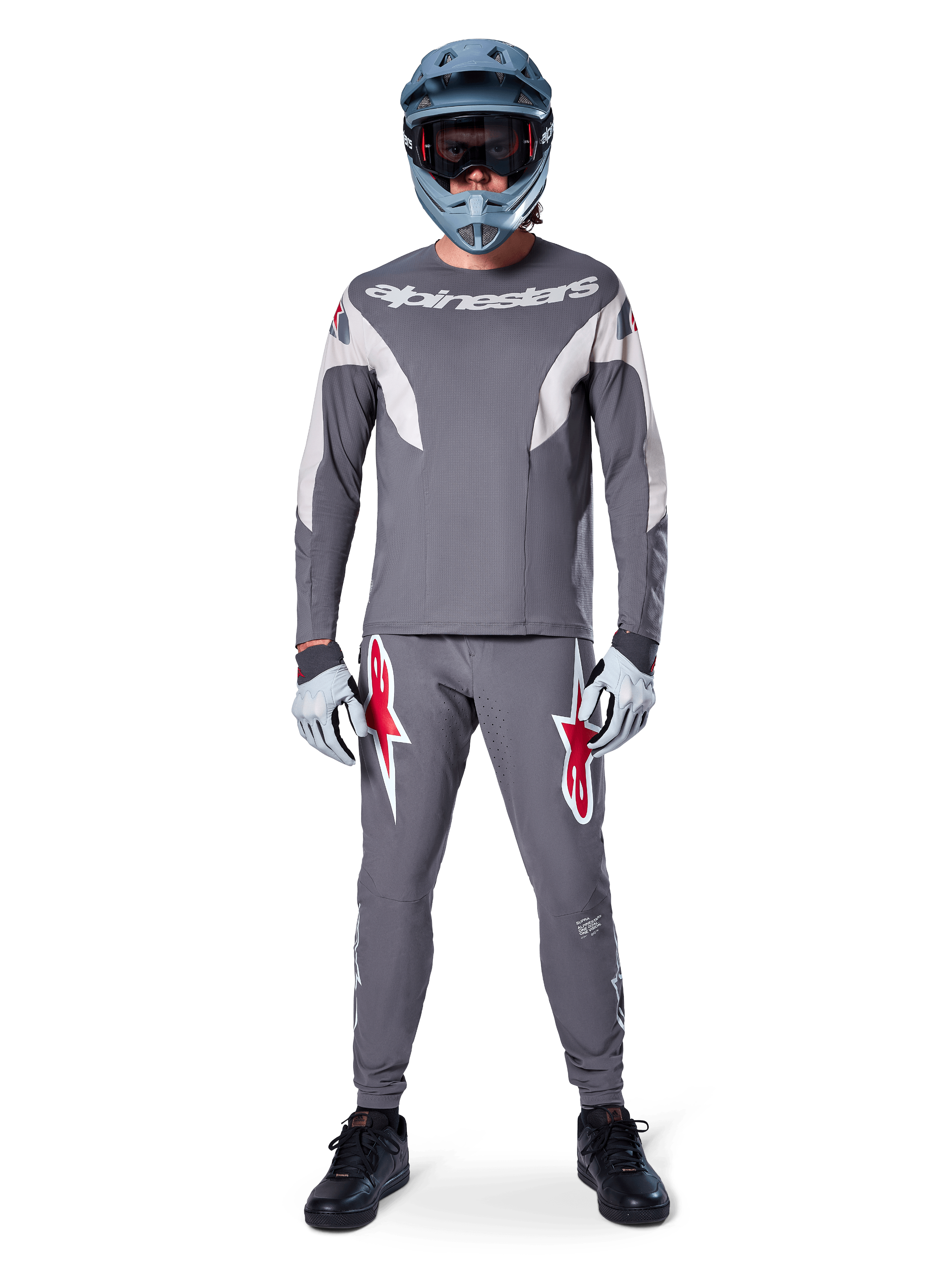 Rytter iført Alpinestars A-Supra Race Jersey - langærmet i mørkegrå, koordineret med matchende grå bukser med markante røde stjernelogoer, grå hjelm med goggles og lysegrå handsker, komplet MTB-racerudstyr til performance off-road cykling