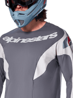 Alpinestars A-Supra Race langærmet trøje, MTB-trøje, mørkegrå med hvid racing-grafik og hvidt Alpinestars-logo, båret med en lyseblå full-face hjelm og goggles, mikroperforeret stof til terrænkørsel