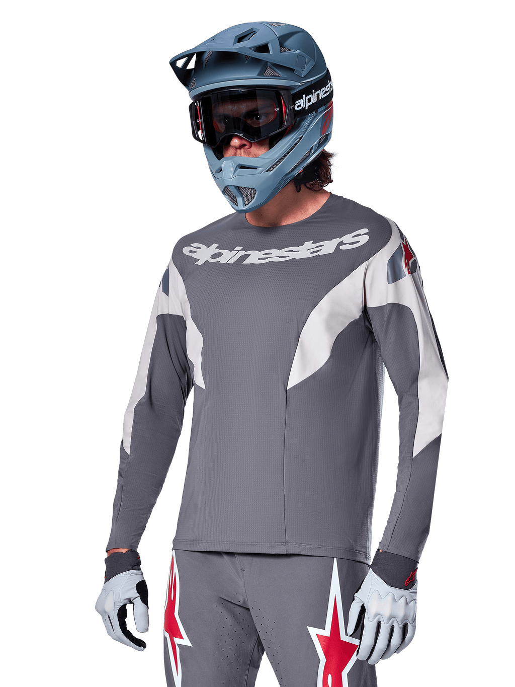 Alpinestars A-Supra Race Jersey - langærmet, mørkegrå med hvide og røde accenter, grafik i racing-stil, båret med matchende grå bukser, blå full-face hjelm og hvide handsker, professionelt MTB- og downhill-racerudstyr