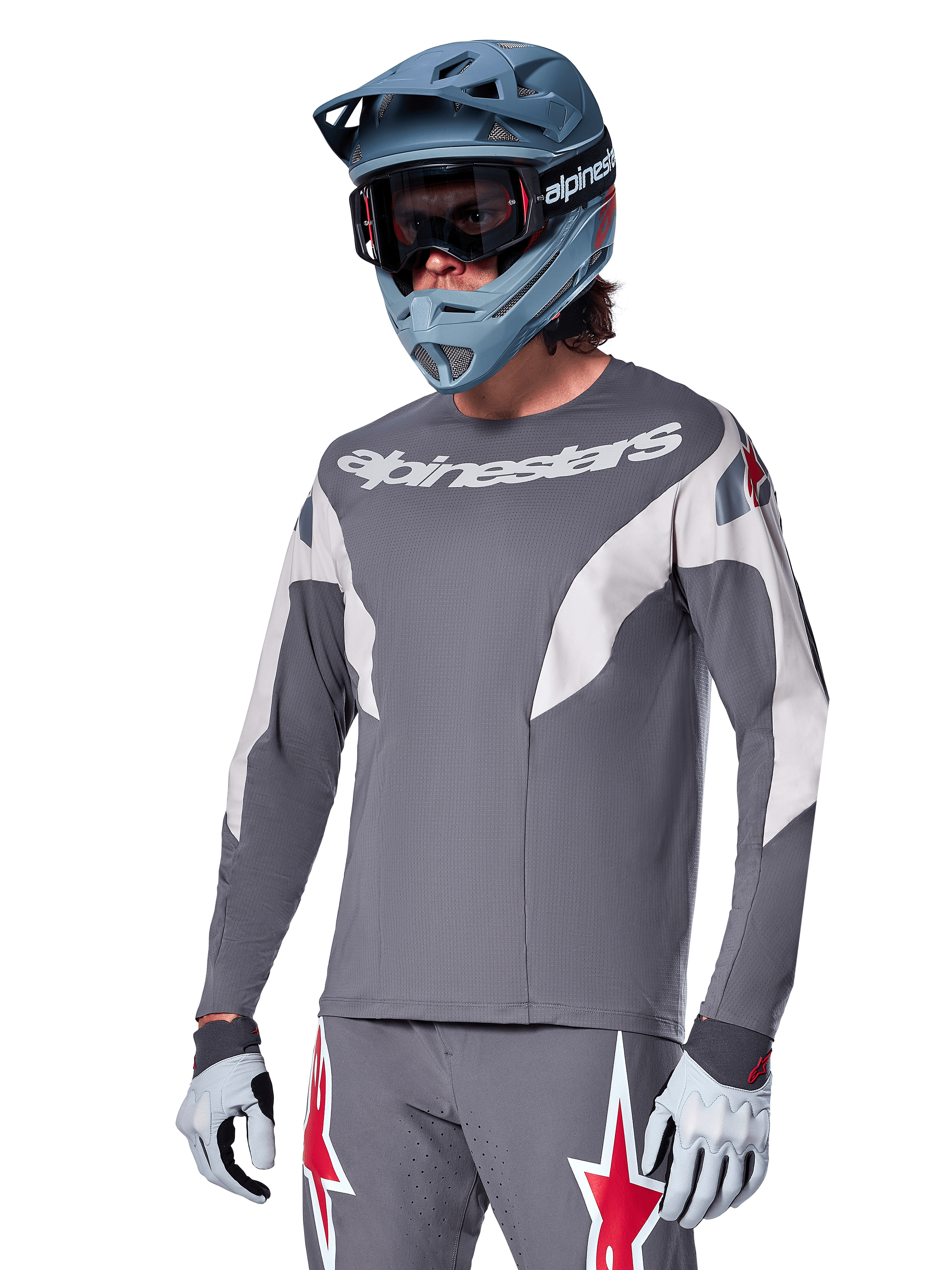 Alpinestars A-Supra Race Jersey - langærmet, mørkegrå med hvide og røde accenter, grafik i racing-stil, båret med matchende grå bukser, blå full-face hjelm og hvide handsker, professionelt MTB- og downhill-racerudstyr