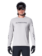 Alpinestars A-Dura Switch Long Sleeve Jersey, Light Gray, features dark gray chest wordmark and sleeve star logos, worn by a rider with a black MTB helmet and gloves, performance cycling apparel for trail riding
