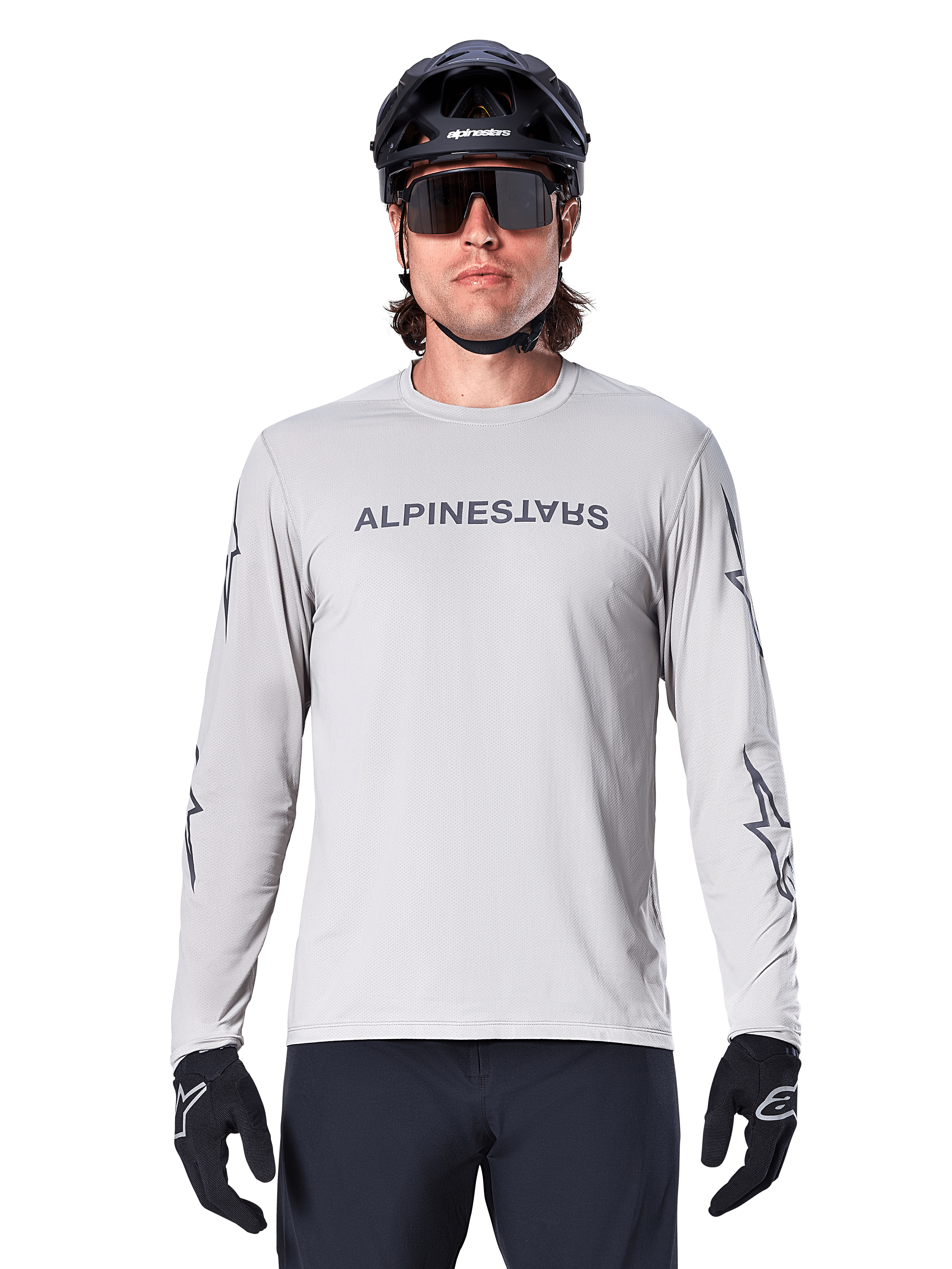 Alpinestars A-Dura Switch Long Sleeve Jersey, Light Gray, features dark gray chest wordmark and sleeve star logos, worn by a rider with a black MTB helmet and gloves, performance cycling apparel for trail riding