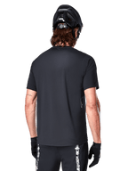 Alpinestars A-Dura Switch Short Sleeve Jersey, Black, rear view on a model wearing a black cycling helmet and MTB shorts, highlighting the regular fit and longer drop tail designed for mountain biking.