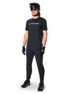 Alpinestars A-Dura Switch Short Sleeve Jersey, Black, worn by model with matching black MTB pants, helmet, and gloves, featuring a white Alpinestars wordmark on the chest, performance mountain bike apparel