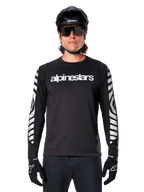 Male rider wearing Alpinestars A-Dura Dri Oscar Long Sleeve Jersey, Black Reflective, featuring white alpinestars wordmark on chest and silver reflective graphics on sleeves, paired with black MTB helmet, sunglasses, and black gloves, performance cycling gear