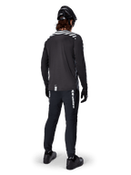 Mountain bike rider wearing the Alpinestars A-Dura Dri Oscar Long Sleeve Jersey in Black Reflective, viewed from behind, paired with black technical pants, helmet, and gloves, featuring reflective stripe graphics on the shoulders and a longer drop tail for off-road cycling.