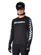 Alpinestars A-Dura Dri Oscar Long Sleeve Jersey, MTB Cycling Jersey, Black Reflective, featuring a white chest wordmark and bold reflective circular graphics on the sleeves, worn with a black helmet and sunglasses, technical moisture-wicking apparel for off-road mountain biking