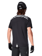 Alpinestars A-Dura Dri Oscar Jersey, Short Sleeve MTB Jersey, Black Reflective, back view on model wearing a cycling helmet and gloves, featuring reflective grey shoulder stripes and a dropped tail, moisture-wicking technical fabric for mountain biking