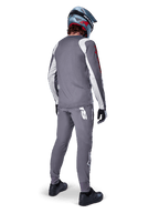Alpinestars A-Supra Astar Jersey, Long Sleeve MTB Jersey, Dark Gray with white sleeve accents and red logo, back view of rider wearing matching gray pants and blue full-face helmet, performance cycling apparel
