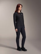 Kvinde iført Alpinestars Stella A-Dura Thermal Jersey, langærmet sort MTB-trøje med hvidt logo på brystet, stylet med matchende sorte bukser og sportssko, studioportræt til teknisk cykeltøj