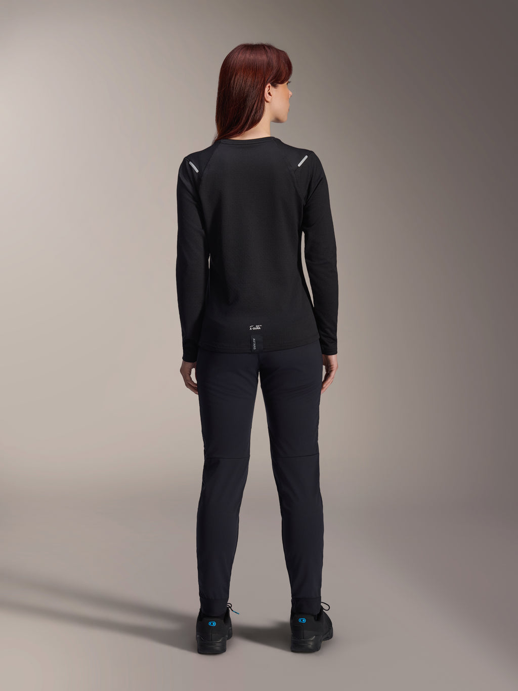 Alpinestars Stella A-Dura Thermal trøje til kvinder, set bagfra, sort, langærmet cykeltrøje med isolerende fleece, kombineret med matchende sorte bukser og sko, med diskret A-Dura-branding nederst på ryggen og reflekterende detaljer på skuldrene, skræddersyet til MTB-kørsel til kvinder.