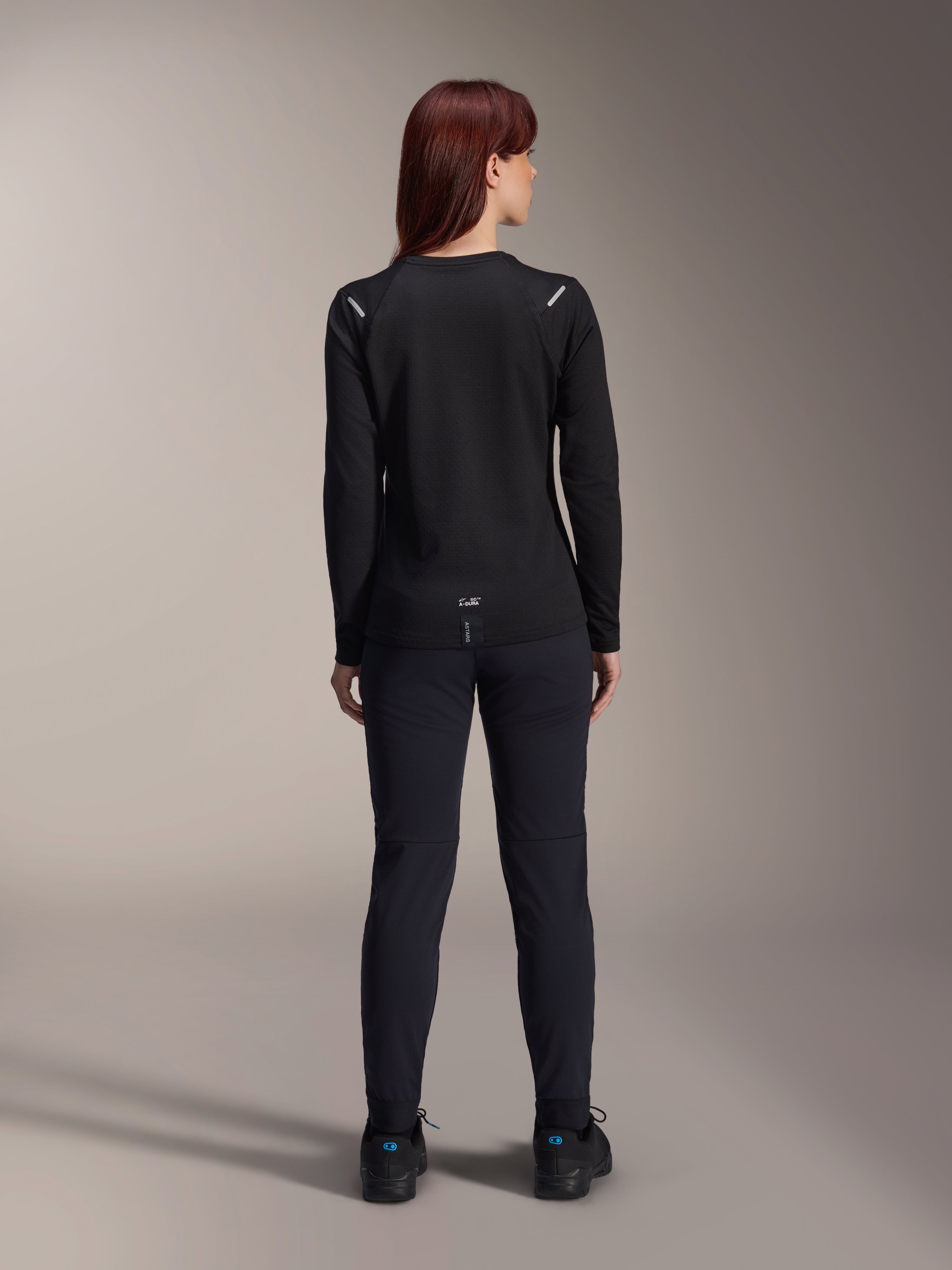Alpinestars Stella A-Dura Thermal trøje til kvinder, set bagfra, sort, langærmet cykeltrøje med isolerende fleece, kombineret med matchende sorte bukser og sko, med diskret A-Dura-branding nederst på ryggen og reflekterende detaljer på skuldrene, skræddersyet til MTB-kørsel til kvinder.