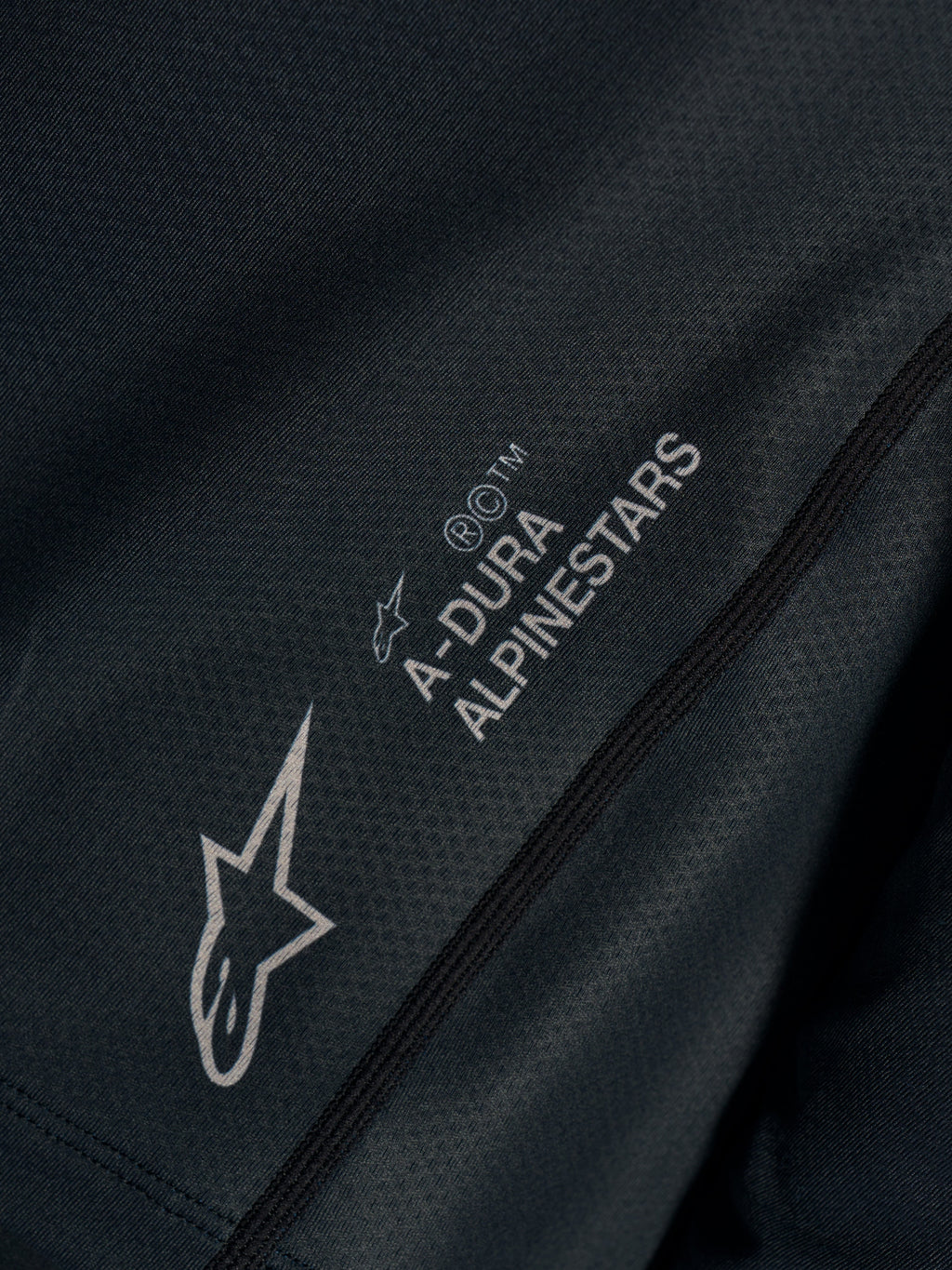 Sort Stella A-Dura Ride trøje, nærbillede af teknisk jacquard-stof med A-DURA ALPINESTARS og Astars-logoer.