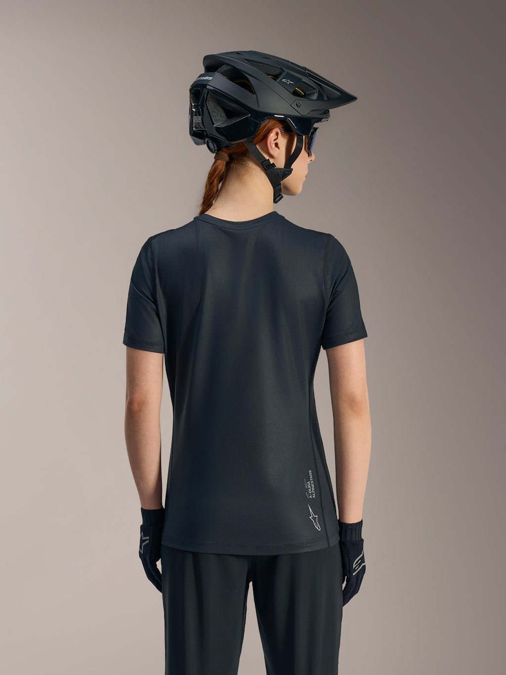 Sort Stella A-Dura Ride kortærmet trøje til kvinder set bagfra, med forlænget rygstykke og Alpinestars-logo.