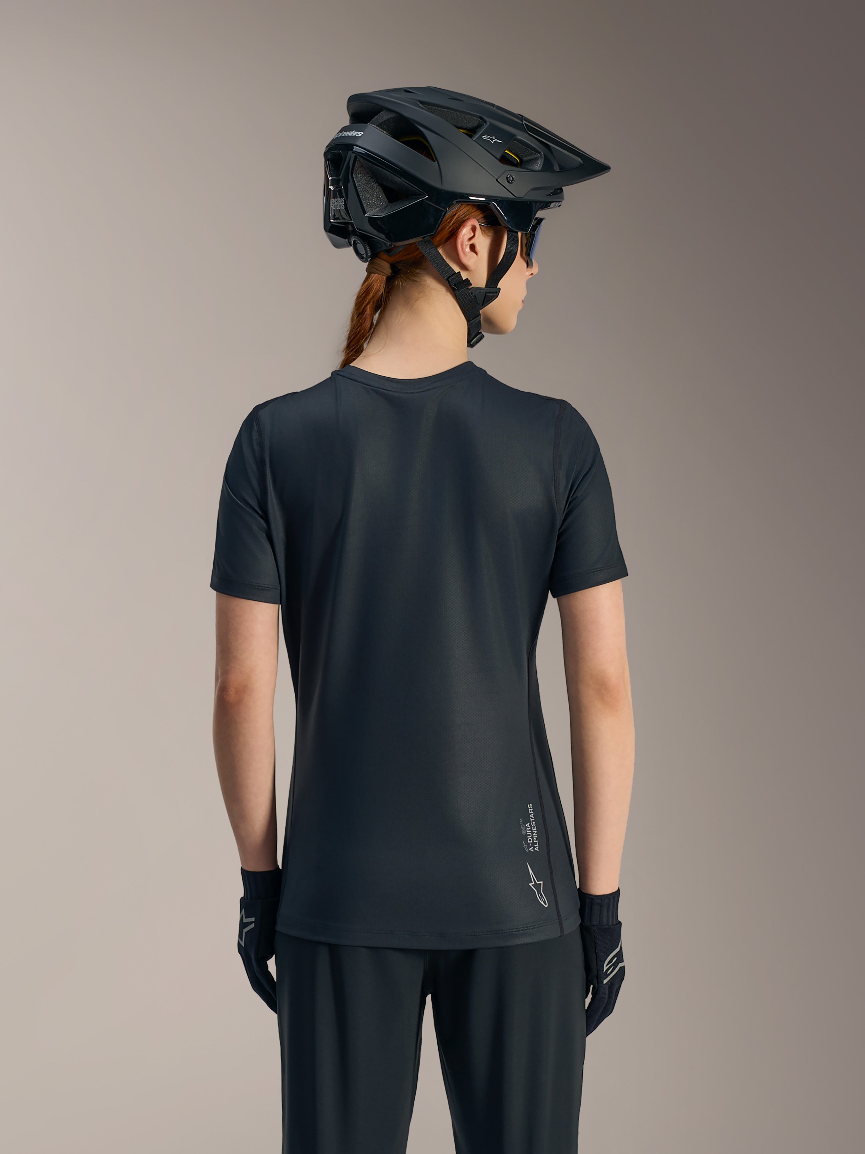 Sort Stella A-Dura Ride kortærmet trøje til kvinder set bagfra, med forlænget rygstykke og Alpinestars-logo.
