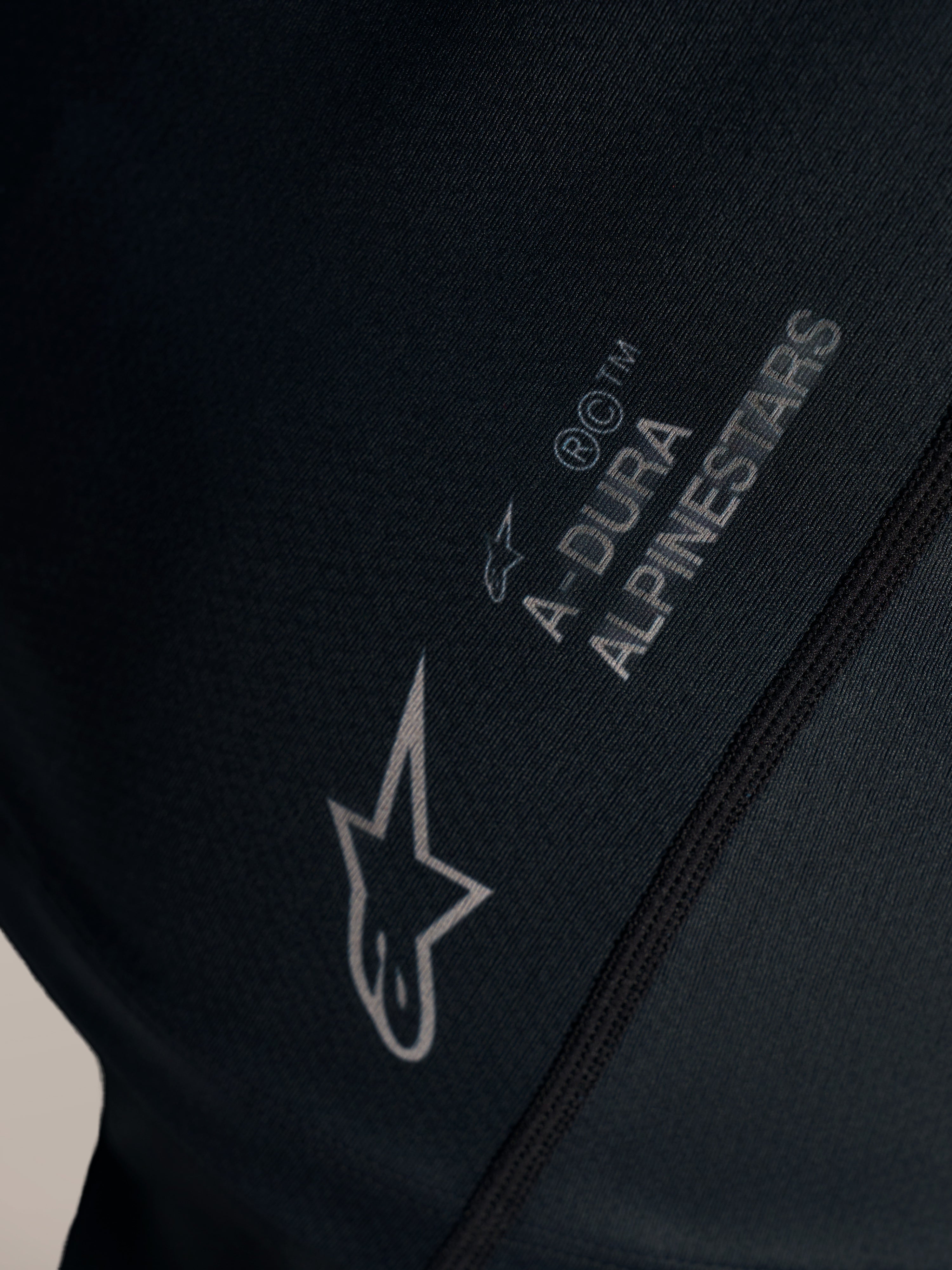 Sort Stella A-Dura Ride trøje med hvidt Alpinestars-logo og A-DURA-branding på jacquard-vævet stof.