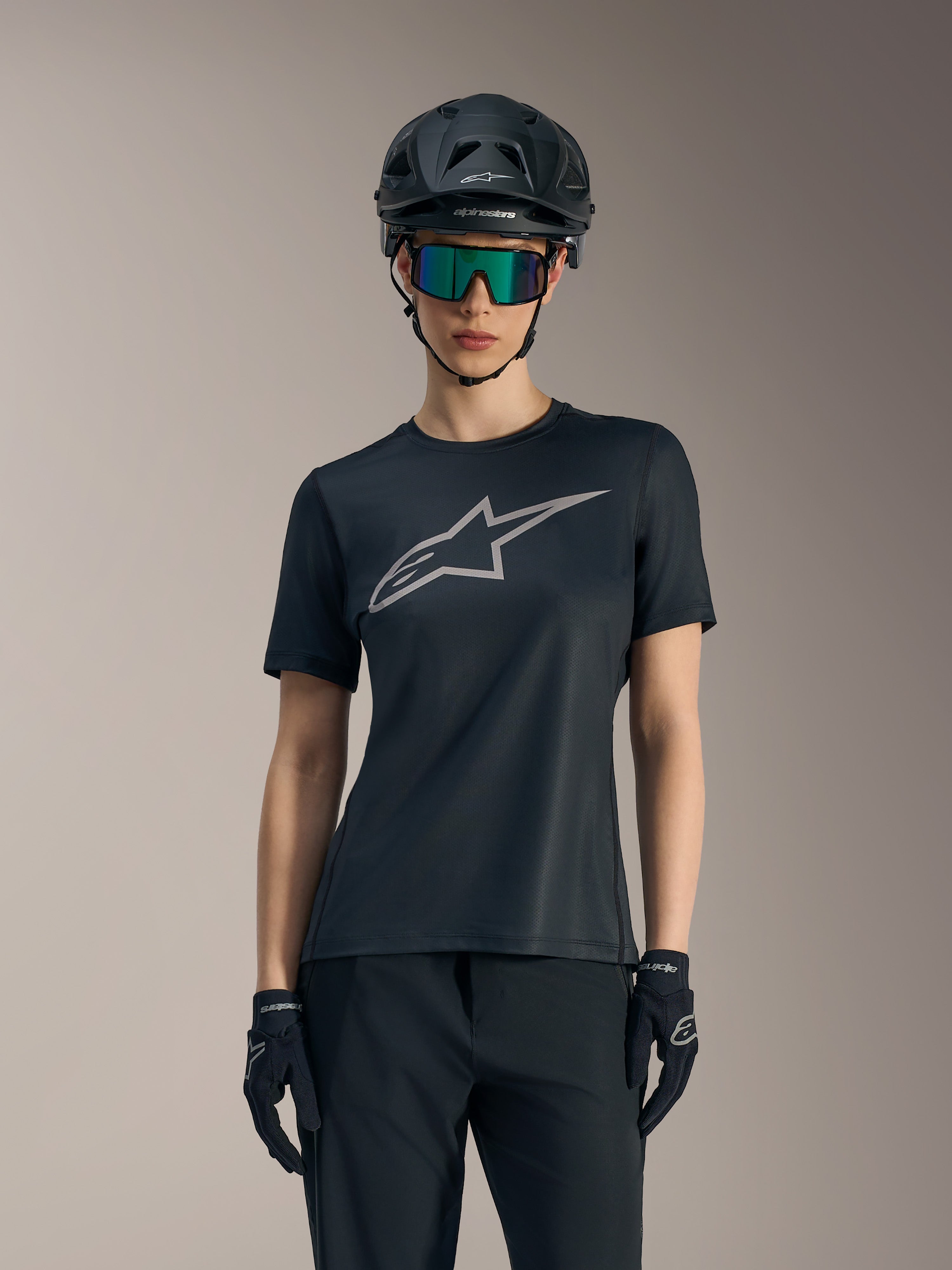 Alpinestars Stella A-Dura Ride-trøje til kvinder, sort med gråt brystlogo, vist med MTB-hjelm og goggles.