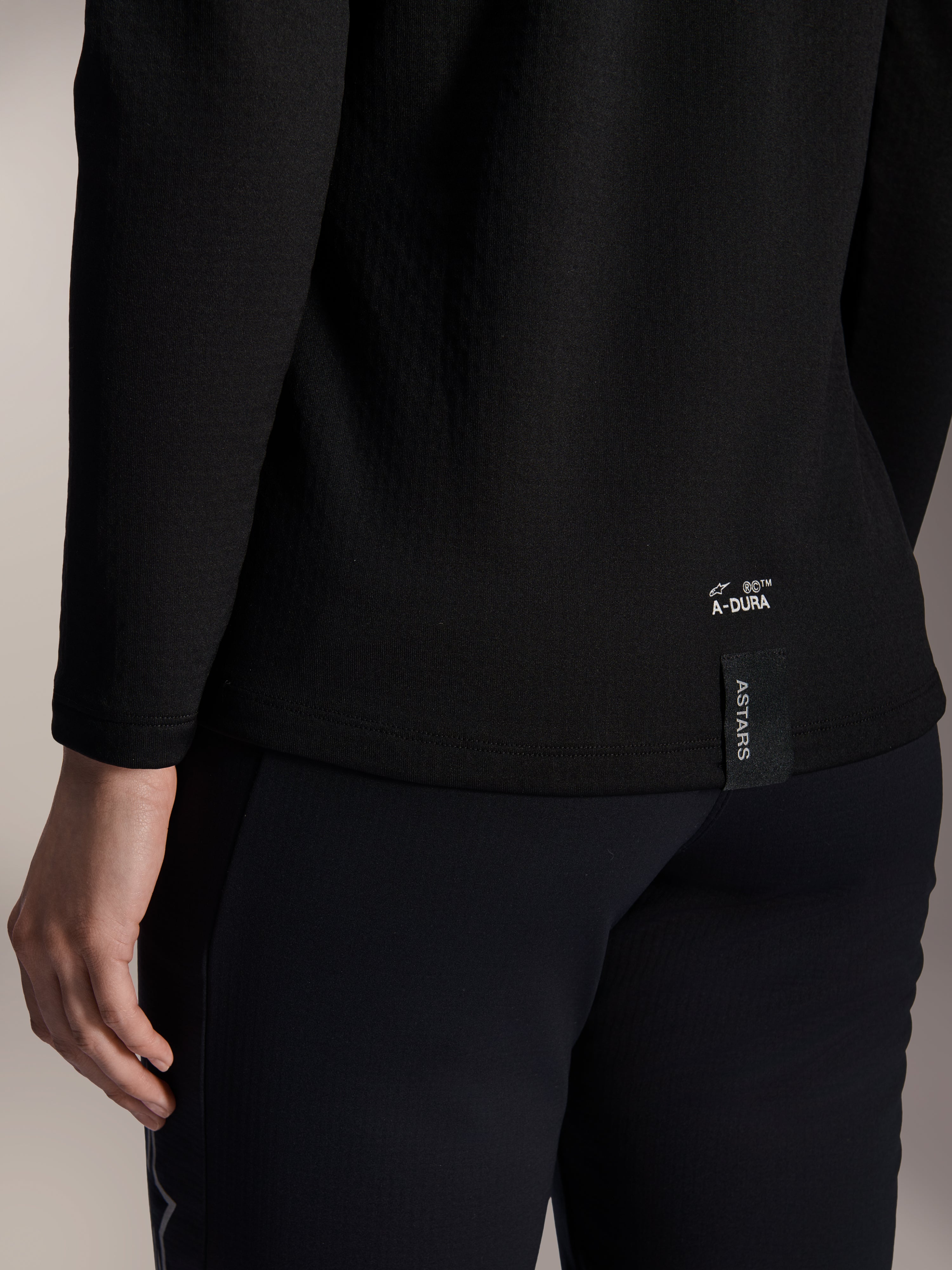 Alpinestars Stella A-Dura termotrøje til kvinder, sort MTB-termotrøje, nærbillede af den nederste kant bagpå med hvidt A-DURA-branding og lodret ASTARS-logotag, designet til mountainbike i koldt vejr