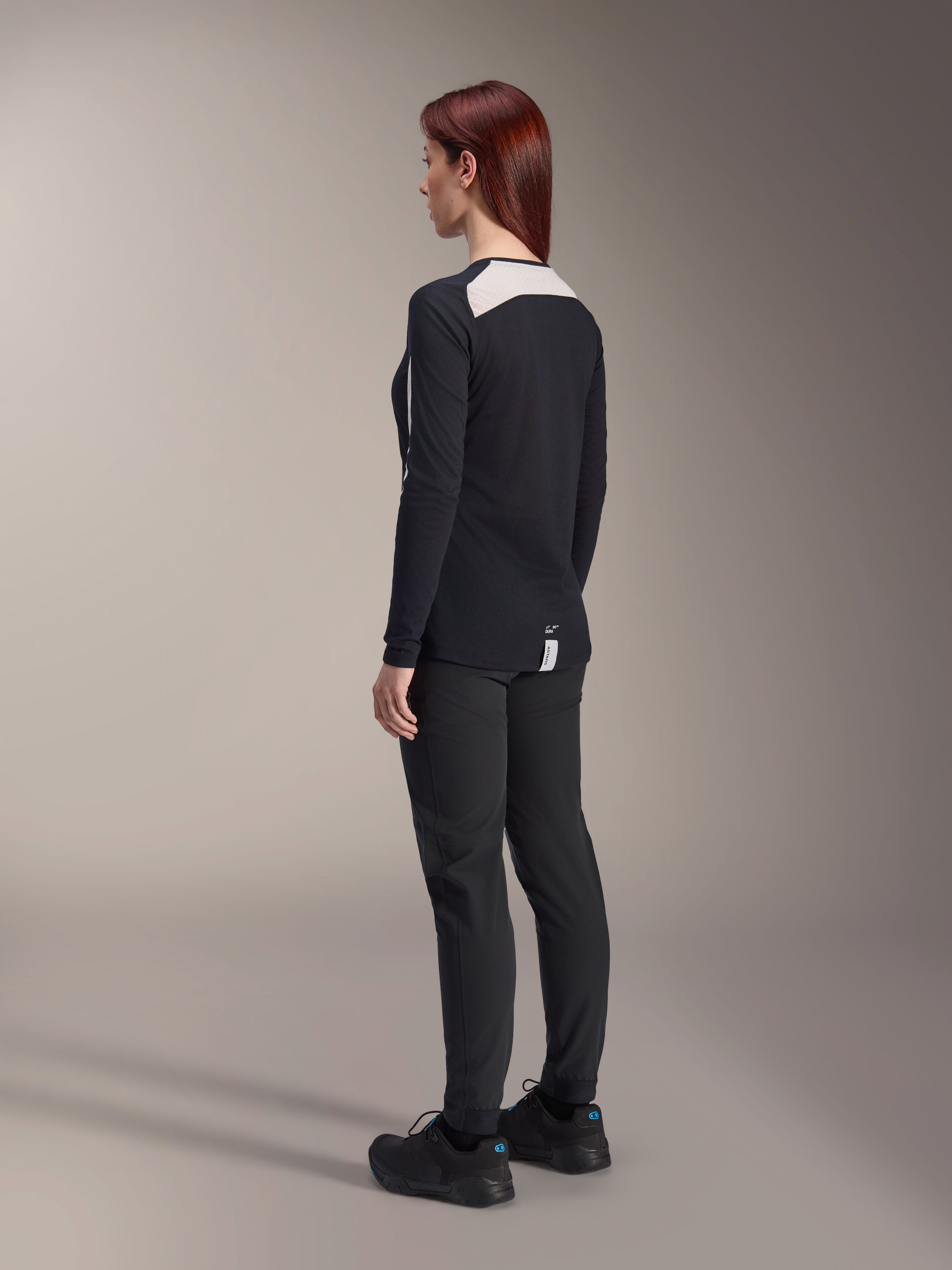 Kvindelig rytter iført Alpinestars Stella A-Dura bukser og Stella A-Dura Elite jersey til kvinder, sort, set bagfra med hvide mesh-skulderpaneler på den langærmede jersey, tekniske bukser med tætsiddende pasform, koordineret mountainbike-udstyr