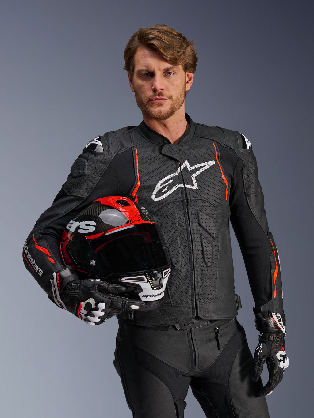 Alpinestars Dusk Airflow læderjakke, sort med Red Fluo-detaljer, båret af en mandlig model, der holder en rød og sort motorcykelhjelm, med perforeret læder for maksimal ventilation og hvidt Alpinestars-logo, motorcykeludstyr til sportskørsel
