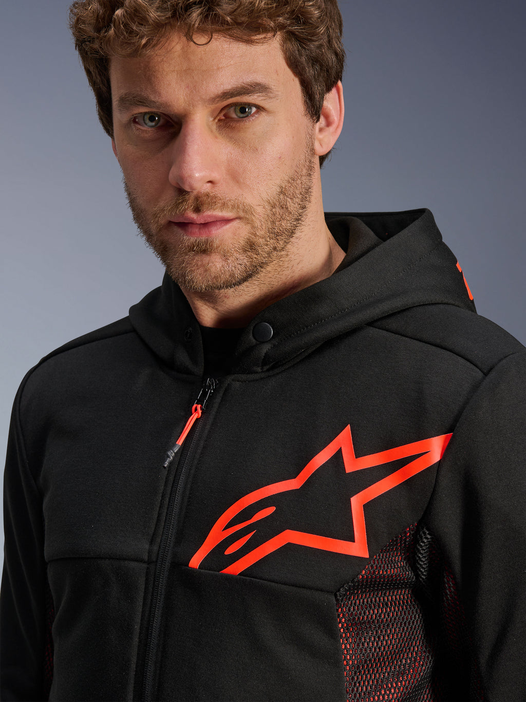 Alpinestars Chrome Air Sport Hoodie, sort og rød fluo, nærbillede af det store rød fluo stjernelogo på brystet, røde mesh-sidepaneler til ventilation, lynlås foran og krave med trykknap, afslappet urbant motorcykeludstyr