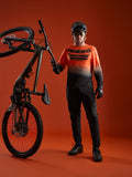 A-Dura ASTARS Jersey 2.0 langærmet trøje i orange-sort gradient med brystlogo, vist med komplet mountainbike-udstyr.