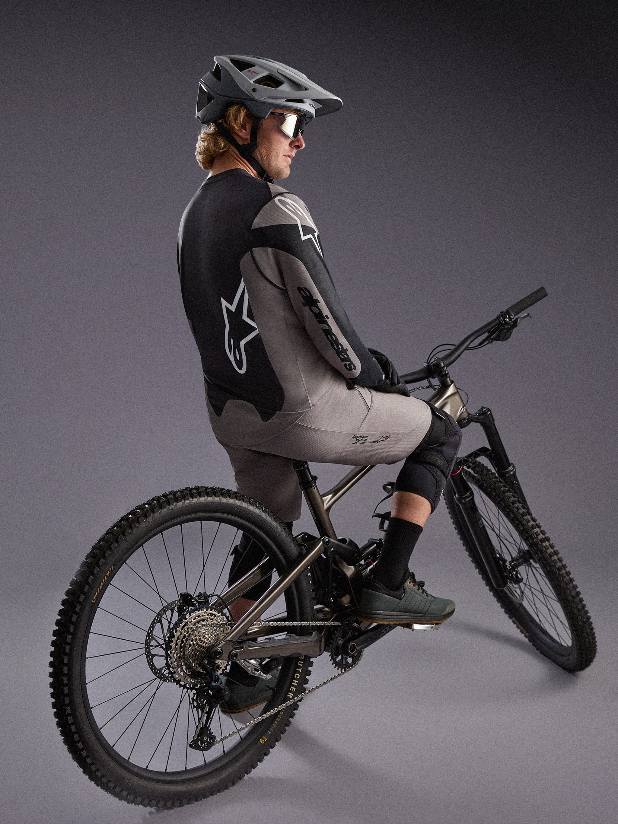 Grå Alpinestars A-Dura Race langærmet trøje på en mountainbiker, med markante logoer og strækbart performance-stof.