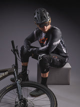 A-Dura Ride Shorts i Black Camo og langærmet jersey, stylet med MTB-udstyr og en Specialized mountainbike.