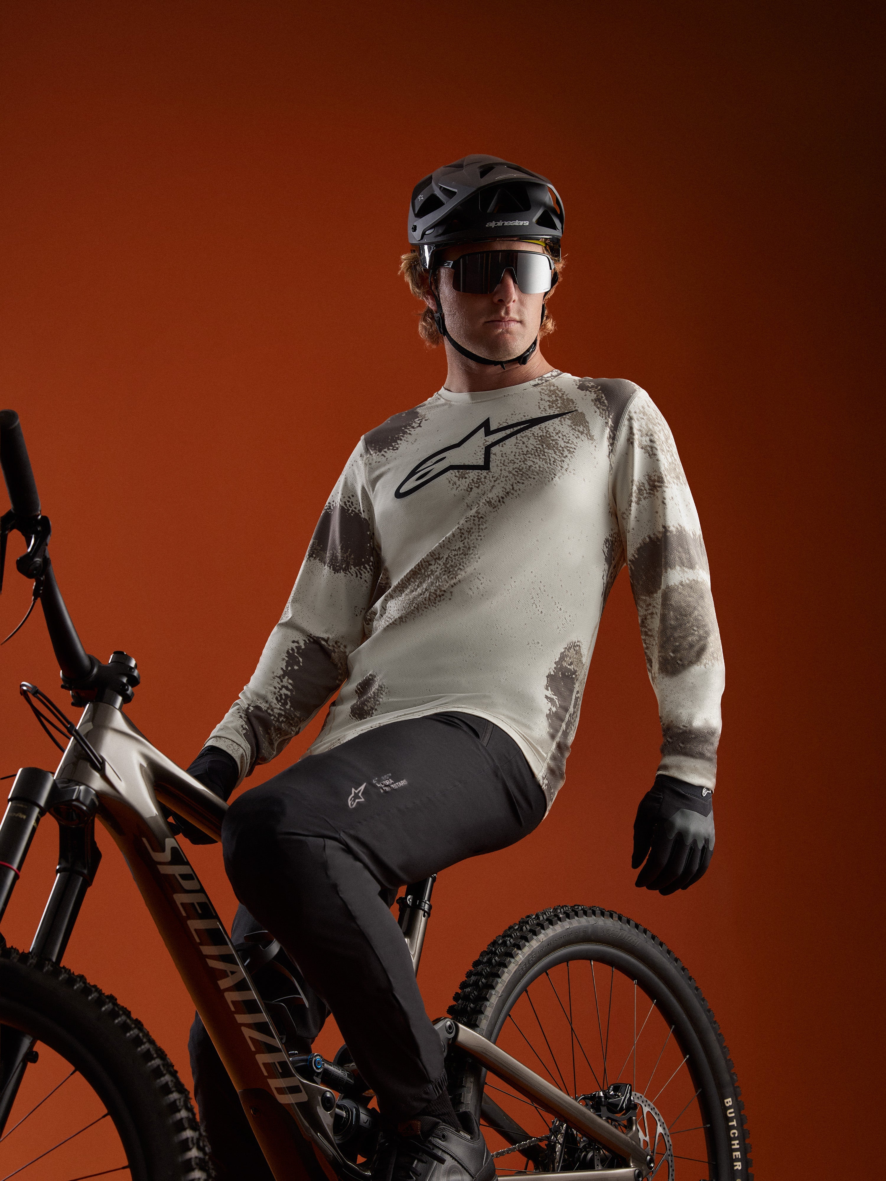 A-Dura Ride Long Sleeve Jersey in Sand Camo with Alpinestars chest logo, worn by an MTB rider on a mountain bike.