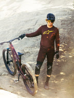Bordeaux Alpinestars A-Dura Ride langærmet trøje med gult logo, båret af rytter på en stenet mountainbikesti.