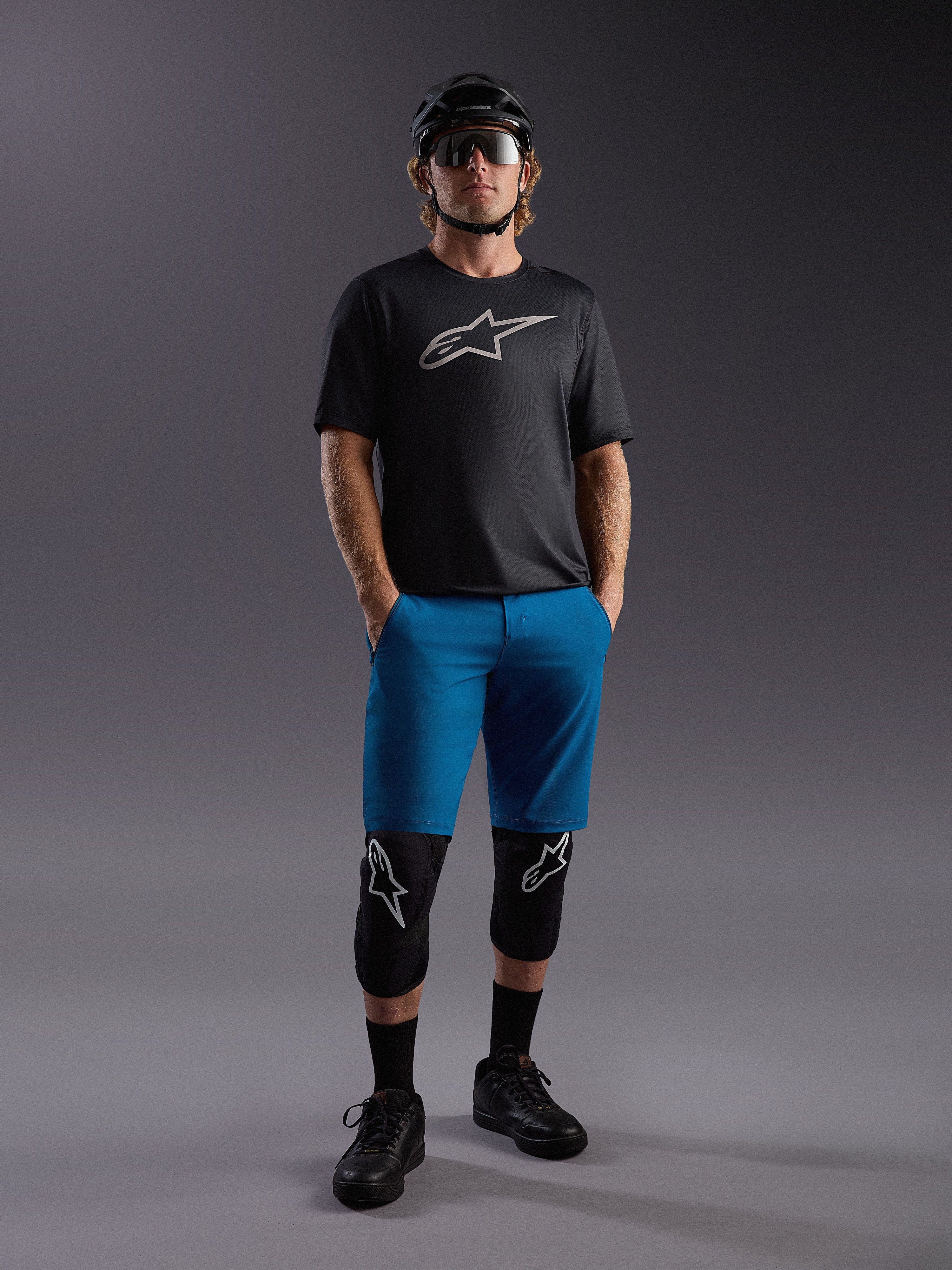 Alpinestars A-Dura Ride SS trøje og blå shorts, komplet mountainbike-outfit med beskyttelsesudstyr og hjelm.