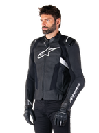 Alpinestars Missile V3 læderjakke, sort og hvid, båret af en mand med sorte kørehandsker, med et fremtrædende hvidt Alpinestars-logo på brystet, eksterne skuldersliders og perforerede paneler for et racer-inspireret look