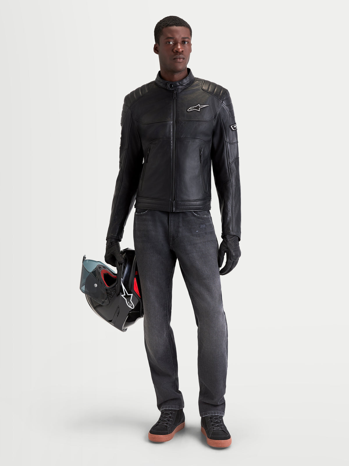 Alpinestars Revern Leather Jacket, men's urban motorcycle leather jacket in black, front view on a model wearing dark jeans and holding a helmet, featuring distressed bovine leather construction and heritage biker styling