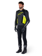 Mandlig model iført Alpinestars Missile V3 Airflow læderjakken i sort, gul fluo og hvid, stylet med sorte kørehandsker, bukser og støvler, der fremviser det perforerede læderdesign og den racing-inspirerede æstetik.