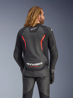 Alpinestars GP Force V2 læderjakke, sort og fluorød, set bagfra på en model, med hvidt Alpinestars-logo og 'RACING AHEAD'-tekst, kombineret med sorte motorcykelbukser og handsker i læder