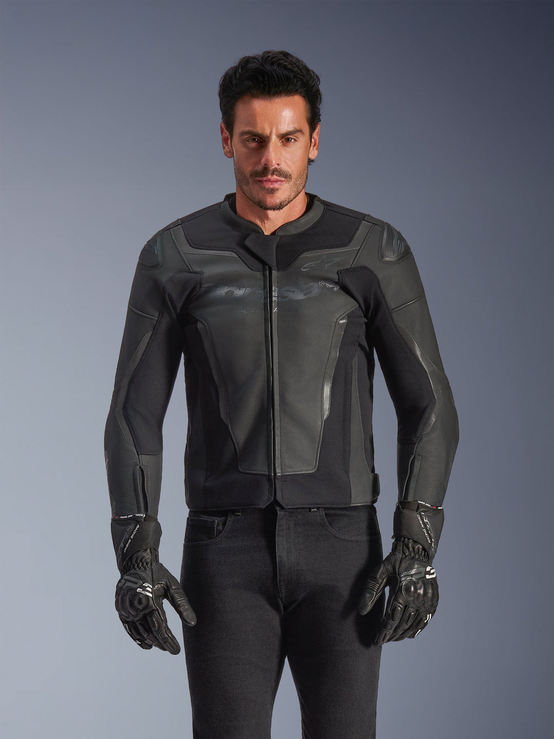 Alpinestars GP Force V2 læderjakke, sort og mørkegrå, motorcykelracerjakke, mand iført slankt, tætsiddende læderdesign med lynlås foran, kombineret med sorte teksturerede handsker, moderne beskyttelsesudstyr, førsteklasses læderkonstruktion