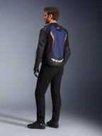 Trekvart profil bagfra af en mandlig model iført Alpinestars GP Force V2 læderjakke i Black Blue Red Fluo, der fremhæver det blå rygpanel med fluorescerende røde detaljer og hvide logoer, stylet med sorte bukser og motorcykelhandsker.