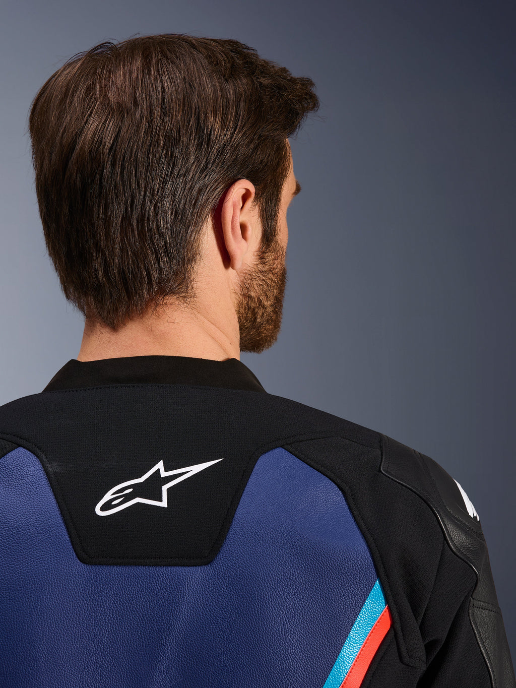 Alpinestars GP Force V2 læderjakke, nærbillede bagfra af nakke og øverste del af skuldrene, hvidt Astars-logo på sort panel, blå læderkonstruktion med fluorescerende røde og lyseblå detaljer, sportskøreudstyr