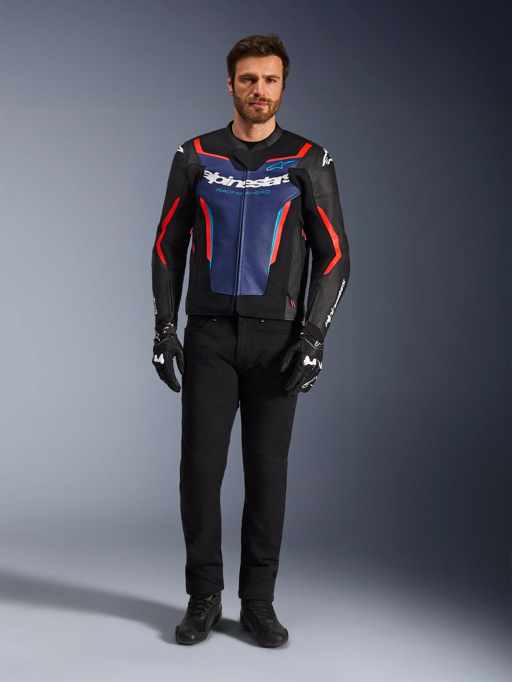 Alpinestars GP Force V2 læderjakke, sort, blå og rød fluo, båret af en mandlig model med sorte bukser og kørehandsker, sportsmotorcykeljakke i okselæder med racer-inspireret design, set forfra