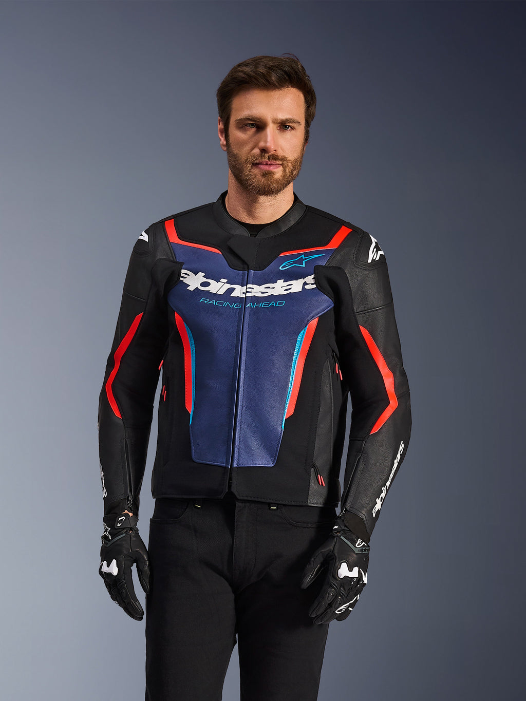 Alpinestars GP Force V2 læderjakke, sort, blå og rød fluo, båret af en mandlig model med sorte handsker og bukser, med et blåt brystpanel med 'Alpinestars Racing Ahead'-tekst, røde detaljer og eksterne skulderskjolde, beskyttelsesudstyr til sportsmotorcykel