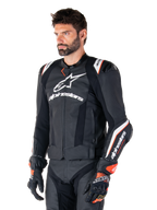 Mandlig model iført Alpinestars Missile V3 Ignition læderjakke, sort med hvide og orange detaljer, fremtrædende hvide logoer, perforerede lædersektioner og beskyttende skulderbeskyttelse, kombineret med racerhandsker for et sport-racing look