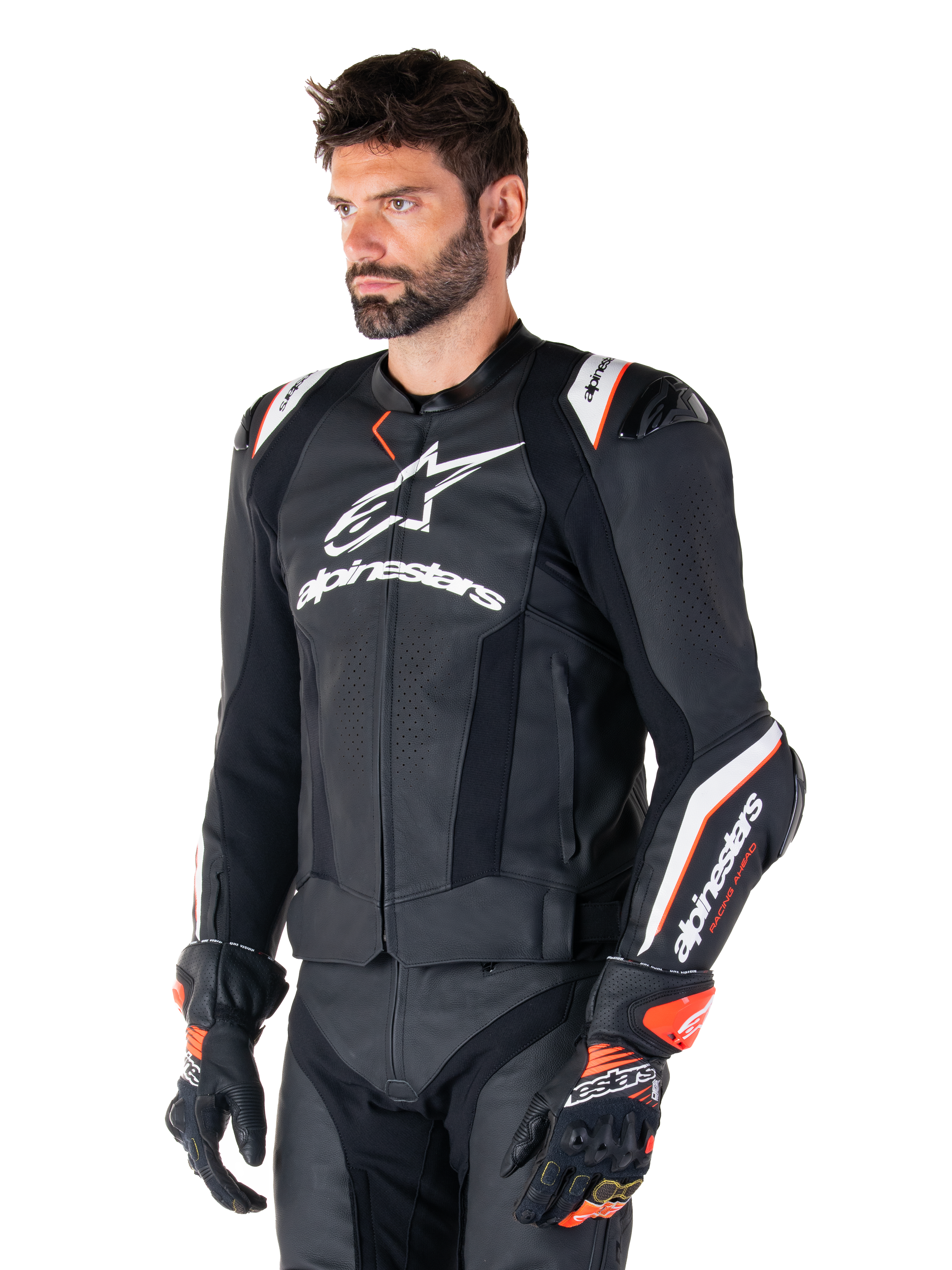 Mandlig model iført Alpinestars Missile V3 Ignition læderjakke, sort med hvide og orange detaljer, fremtrædende hvide logoer, perforerede lædersektioner og beskyttende skulderbeskyttelse, kombineret med racerhandsker for et sport-racing look