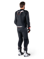 Set bagfra af en kører iført Alpinestars Missile V3 Ignition læderjakke i sort, med en slank sport Aero-hump med hvide og røde detaljer, Alpinestars-branding på den nederste del af ryggen, kombineret med matchende sorte læderbukser og sort-hvide racingstøvler, professionelt sportsudstyr til kørsel